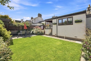A residential property with a well-maintained lawn, a patio with outdoor furniture, and a white exterior wall with windows.