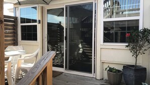 A wooden deck with a table and chairs, a sliding glass door, and potted plants.