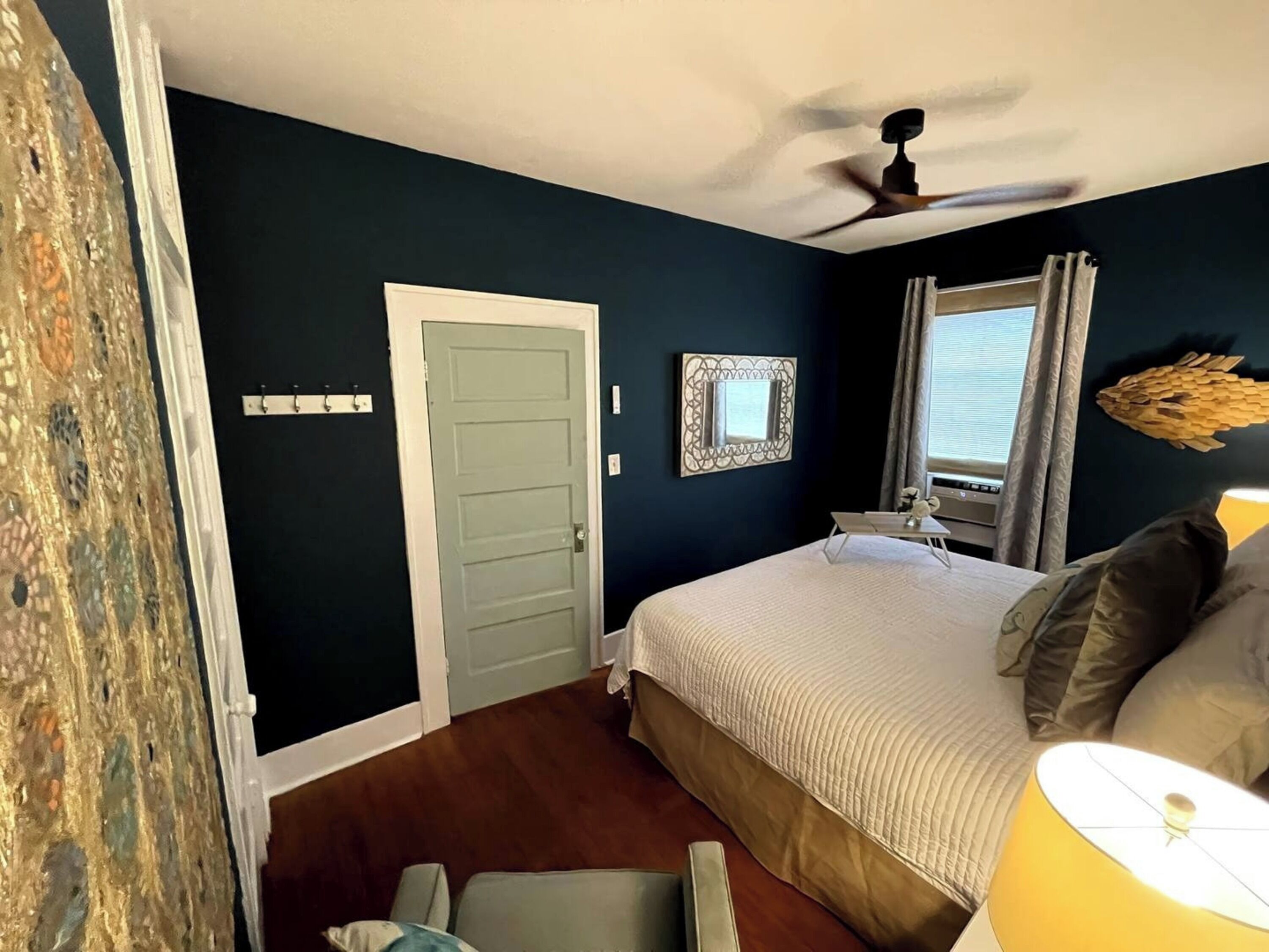 A bedroom with a bed, a ceiling fan, a window with curtains, and a door.