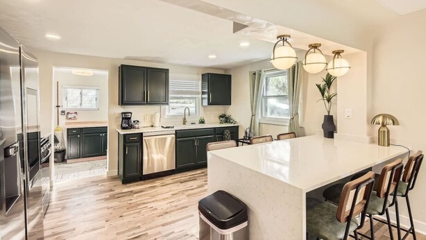 A modern kitchen with dark cabinets, a large island, and bar stools. - The Emerald Haus: Stylish Retreat Near Regis (Denver)