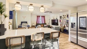 A modern kitchen with a large island, bar stools, a flat-screen TV, and a stainless steel refrigerator. - The Emerald Haus: Stylish Retreat Near Regis (Denver)