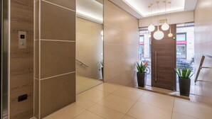 A modern elevator with a digital display, a hallway with a mirror, and a door leading to an outdoor area with plants and a view of the street.