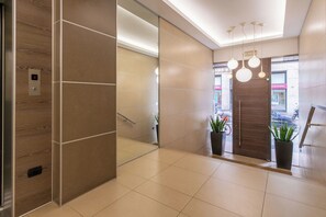 A modern elevator with a digital display, a hallway with a mirror, and a door leading to an outdoor area with plants and a view of the street.