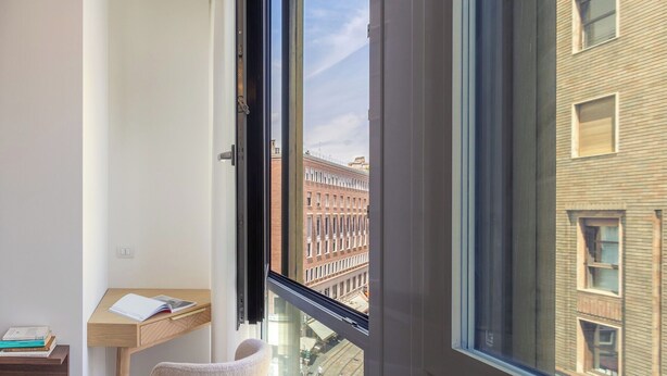 A room with a large window, a desk with a chair, and a view of a brick building.