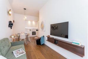 A modern living room with a flat-screen TV, a sofa, a dining area, and a kitchen.