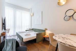 A hotel room with a bed, a desk, a chair, a table, and a TV.