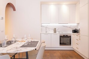 A modern kitchen with white cabinets, a marble countertop, and a built-in oven.