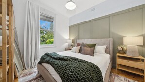 A bedroom with a large bed, a nightstand, a lamp, a window with curtains, and a view of greenery outside. - Bisham Cottage
Fully renovated two bedroom Cottage with a brand new out door Spa (Katoomba)