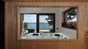 A wooden-paneled room with a large window, a hot tub, and a view of the sea. - Villa Soho - Your Luxury Dream Retreat in Croatia (Starigrad)
