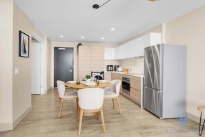 A modern kitchen with a dining area, stainless steel appliances, and light wood cabinetry.