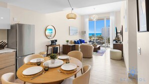Un comedor moderno con una mesa redonda para cuatro personas, un refrigerador y vista al océano a través de amplios ventanales.