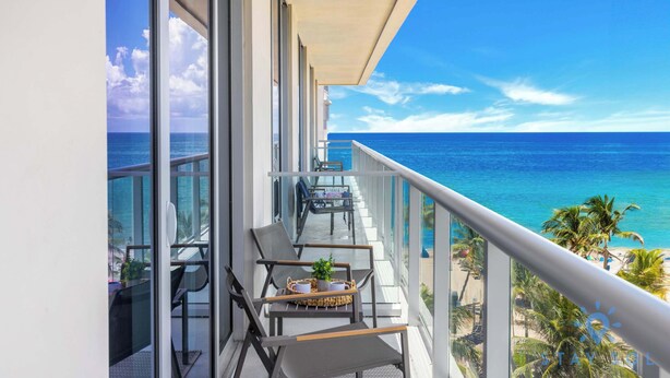 Un balcón con vista al océano, amoblado con sillas y una mesa, y una barandilla.