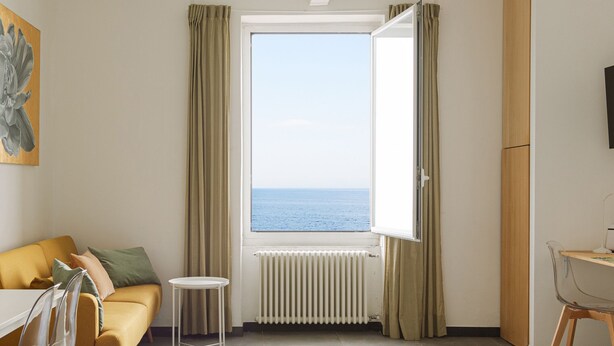 A room with a view of the sea, a sofa, a small table, and a radiator.