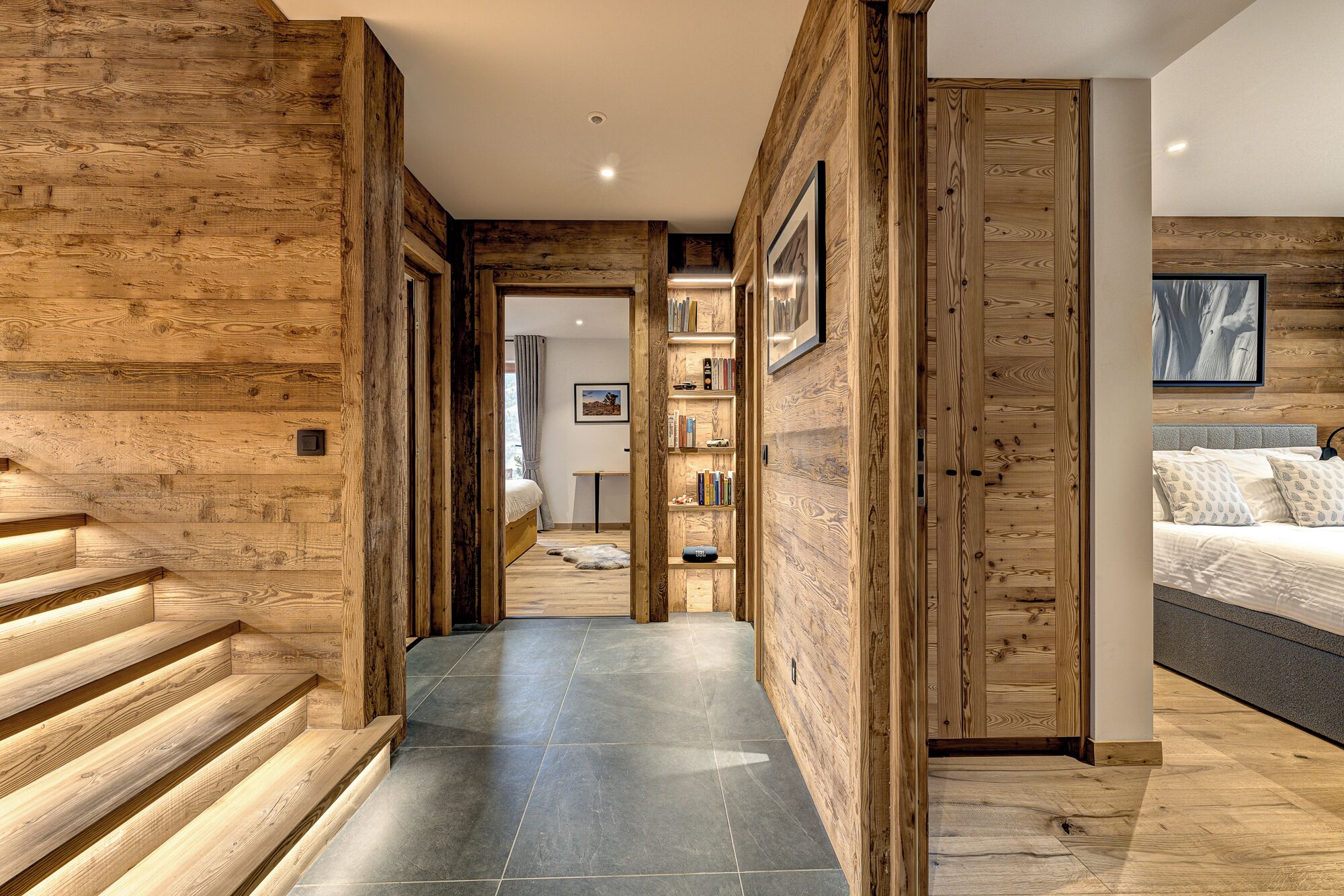 A modern interior with wooden paneling, a staircase, a hallway leading to a bedroom, and a bookshelf.