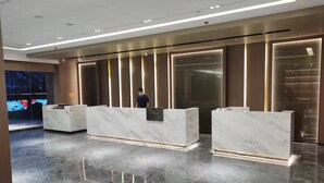 Un moderno vestíbulo de hotel con mostradores de recepción de mármol, una pantalla digital y un suelo limpio y reflectante.