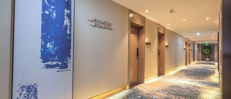 A hotel corridor with a modern design, including a large abstract artwork on the wall, a patterned floor, and a series of doors leading to rooms.