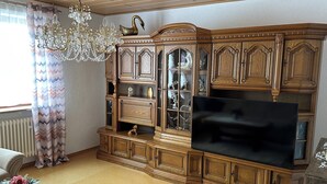 Un salon avec une grande armoire en bois, un lustre et un téléviseur à écran plat.