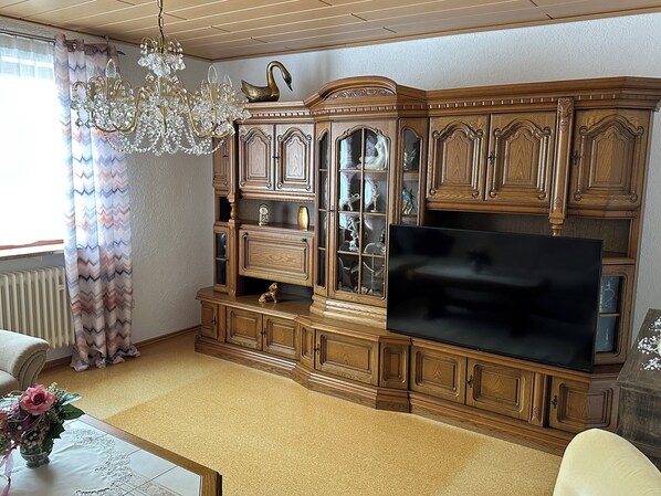 A living room with a large wooden cabinet, a chandelier, and a flat-screen TV.