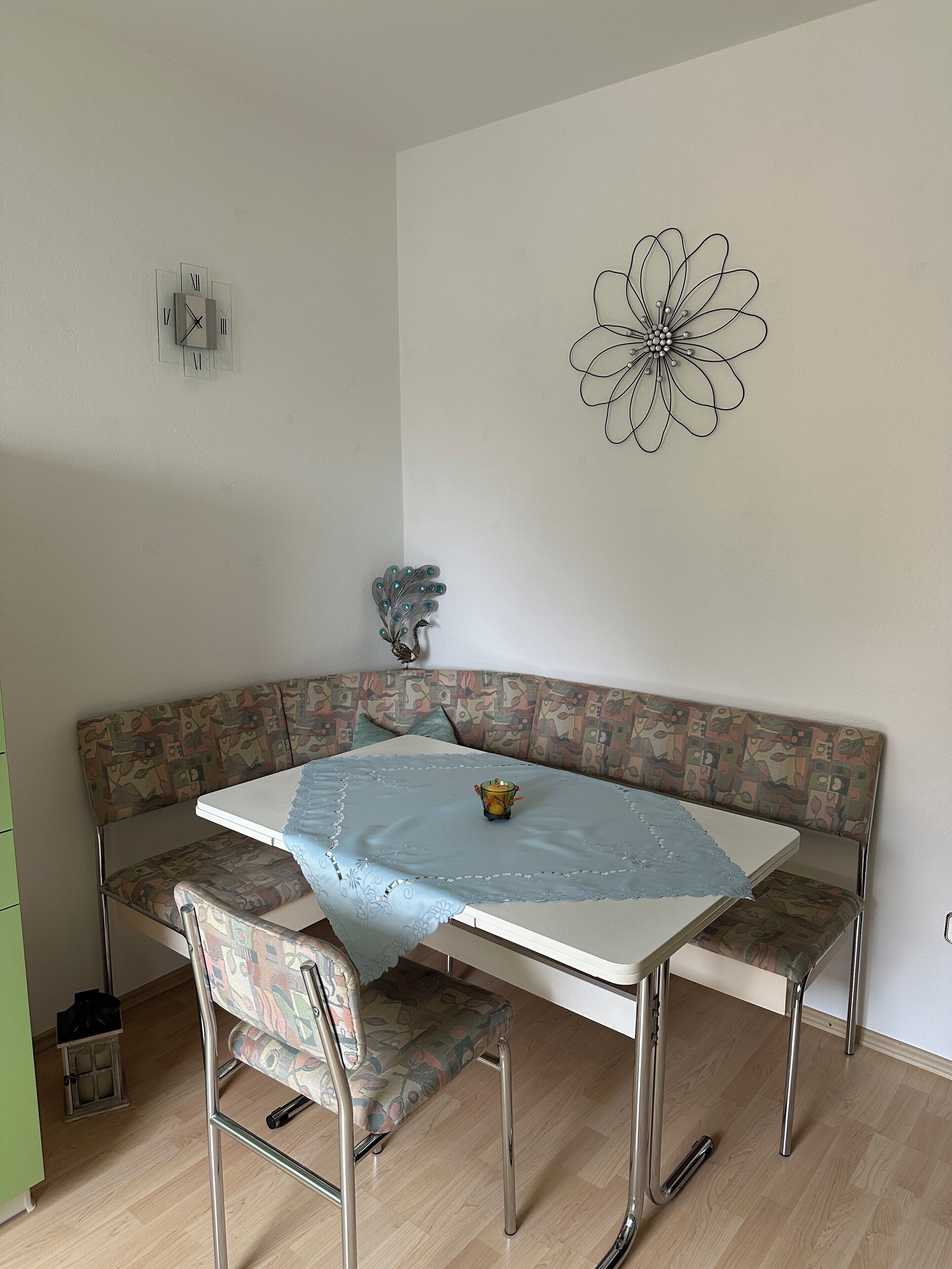 Un rincón comedor con un banco de esquina, una mesa con mantel de encaje y una decoración floral en la pared.