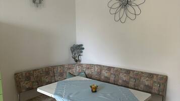 Un rincón comedor con un banco de esquina, una mesa con mantel de encaje y una decoración floral en la pared.