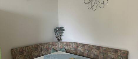 A dining area with a corner bench, a table with a lace tablecloth, and a wall-mounted flower decoration.