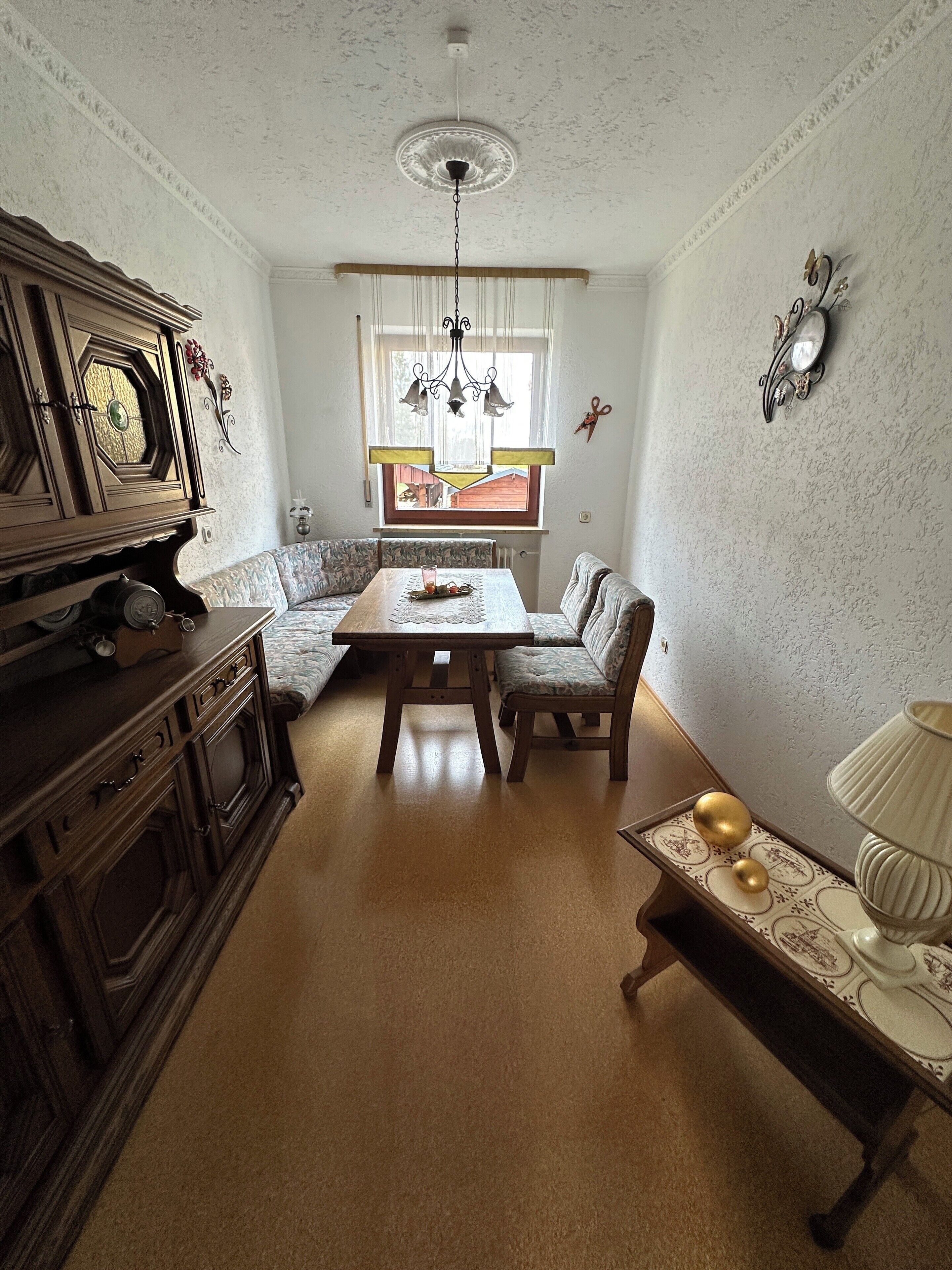 Une pièce comprenant une table à manger en bois, deux chaises, un canapé, un meuble et une fenêtre avec des rideaux.