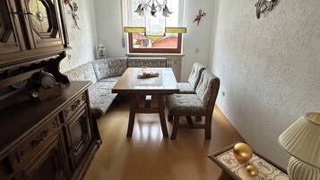 Une pièce comprenant une table à manger en bois, deux chaises, un canapé, un meuble et une fenêtre avec des rideaux.