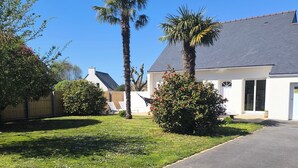 Una calle residencial con camino de entrada pavimentado, césped y una casa blanca con techo gris.