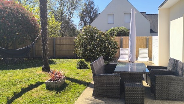 Un patio con mobiliario de mimbre, una mesa y un pequeño jardín.