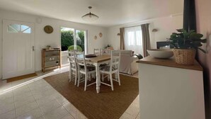Un comedor amplio con una mesa de madera y sillas blancas, una zona de cocina con fregadero y armarios, y un ventanal que proporciona luz natural.
