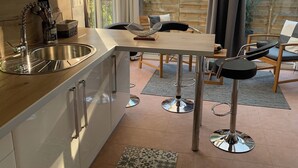 A modern kitchen with a large window, a dining area with a table and chairs, and a small bar stool.