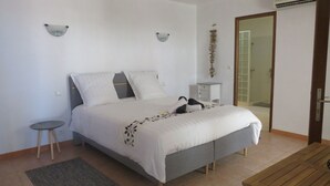 A bedroom with a bed, bedside tables, a small stool, a rug, and a door leading to a bathroom.