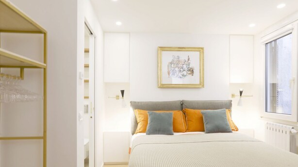 Een slaapkamer met een bed, een lijst met een afbeelding aan de muur en een raam.