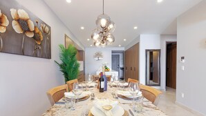 Un comedor con una mesa de mármol, sillas y una lámpara de araña. Hay un cuadro en la pared y una planta en la esquina.