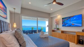 Un dormitorio moderno con una cama grande, televisión y un balcón con vistas al océano.
