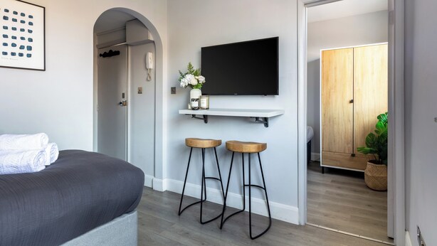 Una moderna camera d'albergo con un letto, due sgabelli da bar, una TV a parete e un armadio in legno.
