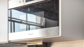 Una cucina moderna con forno a microonde integrato, macchina del caffè, bollitore e una ciotola di frutta su uno scaffale.