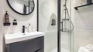 Un bagno moderno con un mobile lavabo bianco, uno specchio rotondo e una zona doccia con pareti in vetro.