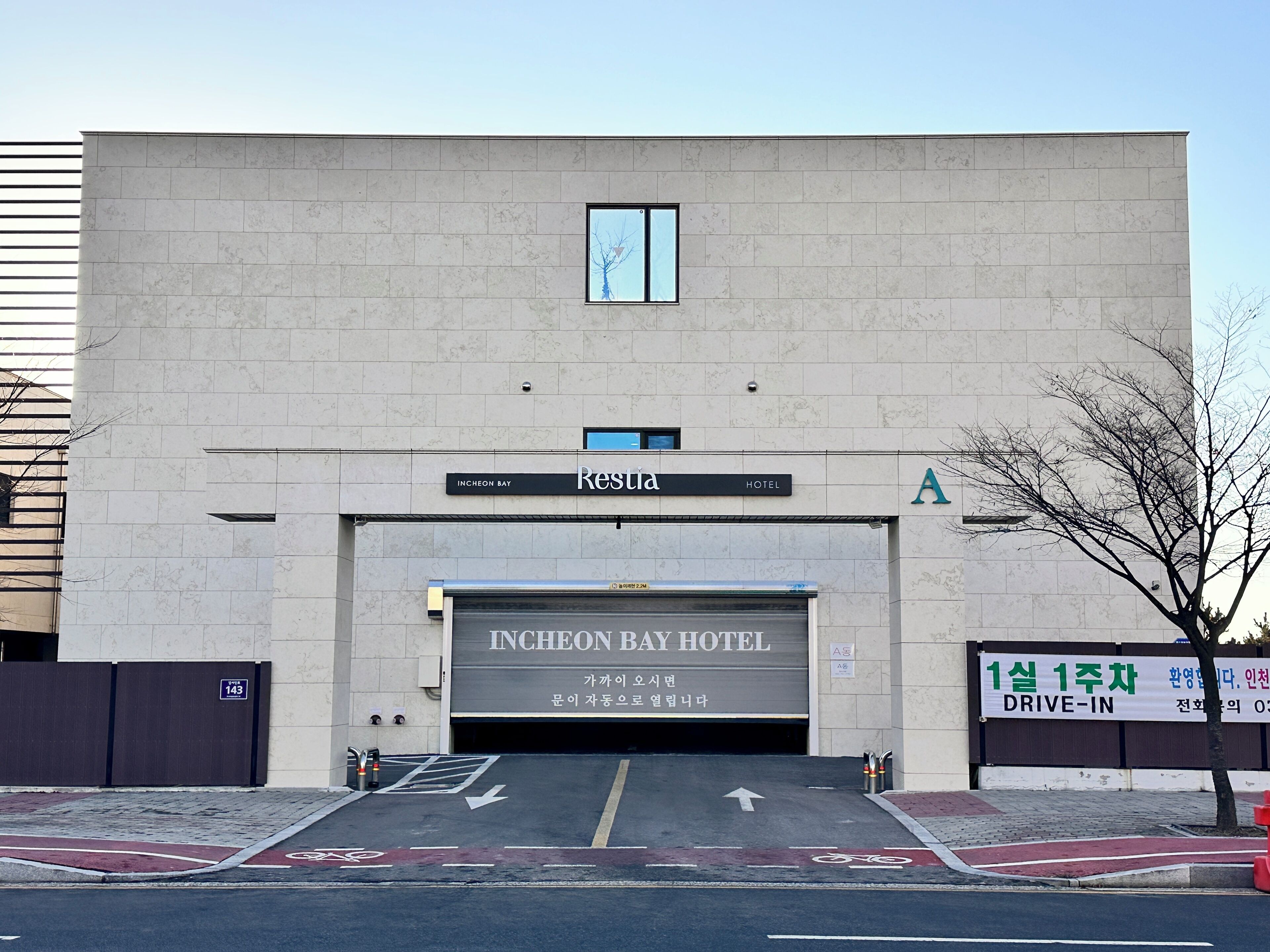 La entrada del Hotel Incheon Bay, con un letrero visible, zona de estacionamiento con acceso directo desde el coche y un carril bici.