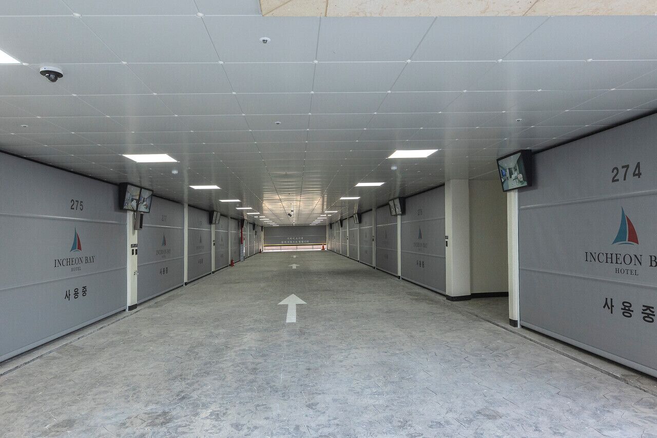A hallway with numbered doors, directional arrows, and a surveillance camera.