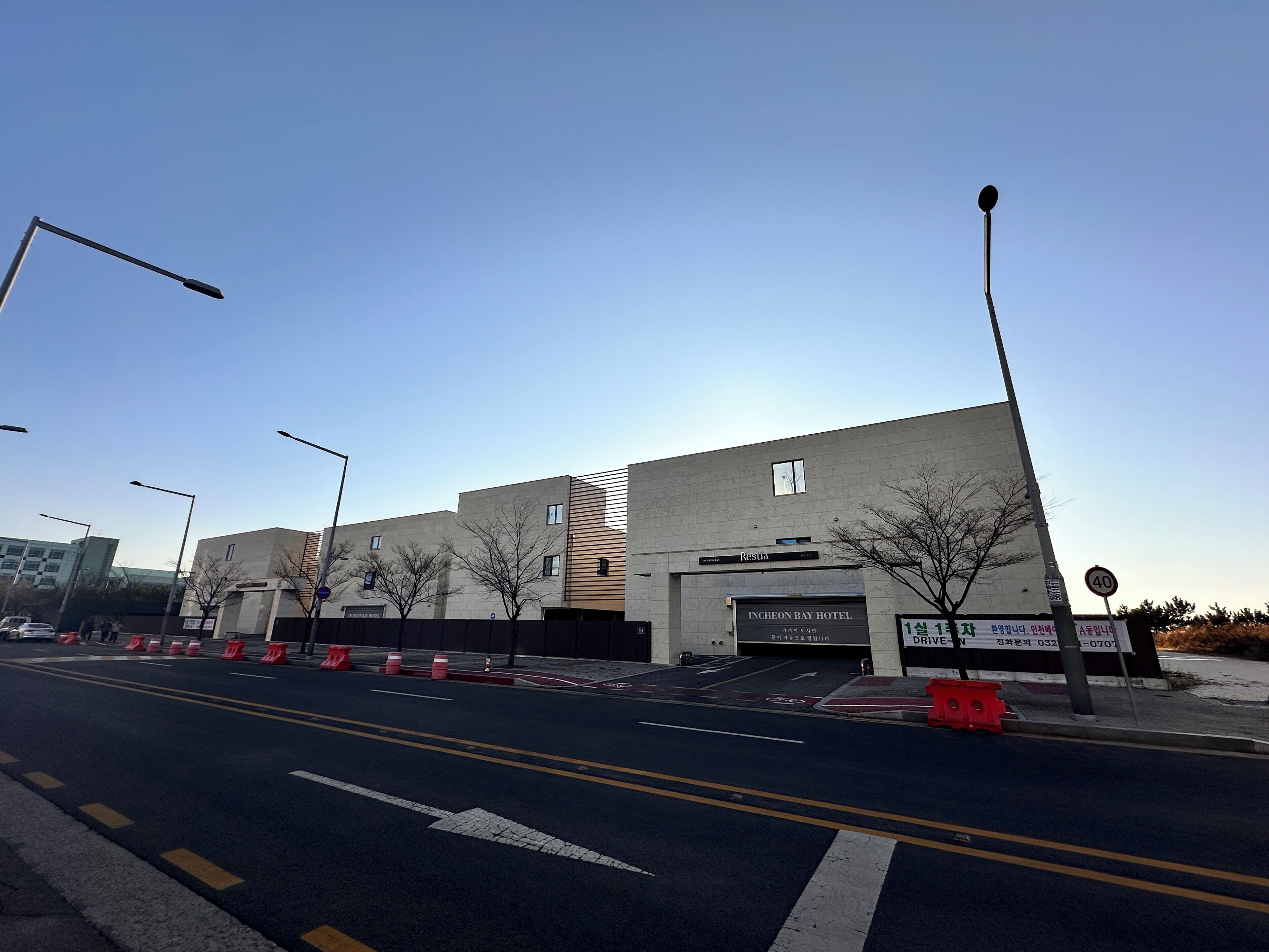 A modern hotel with a flat facade, a visible entrance, and a clear road in front.