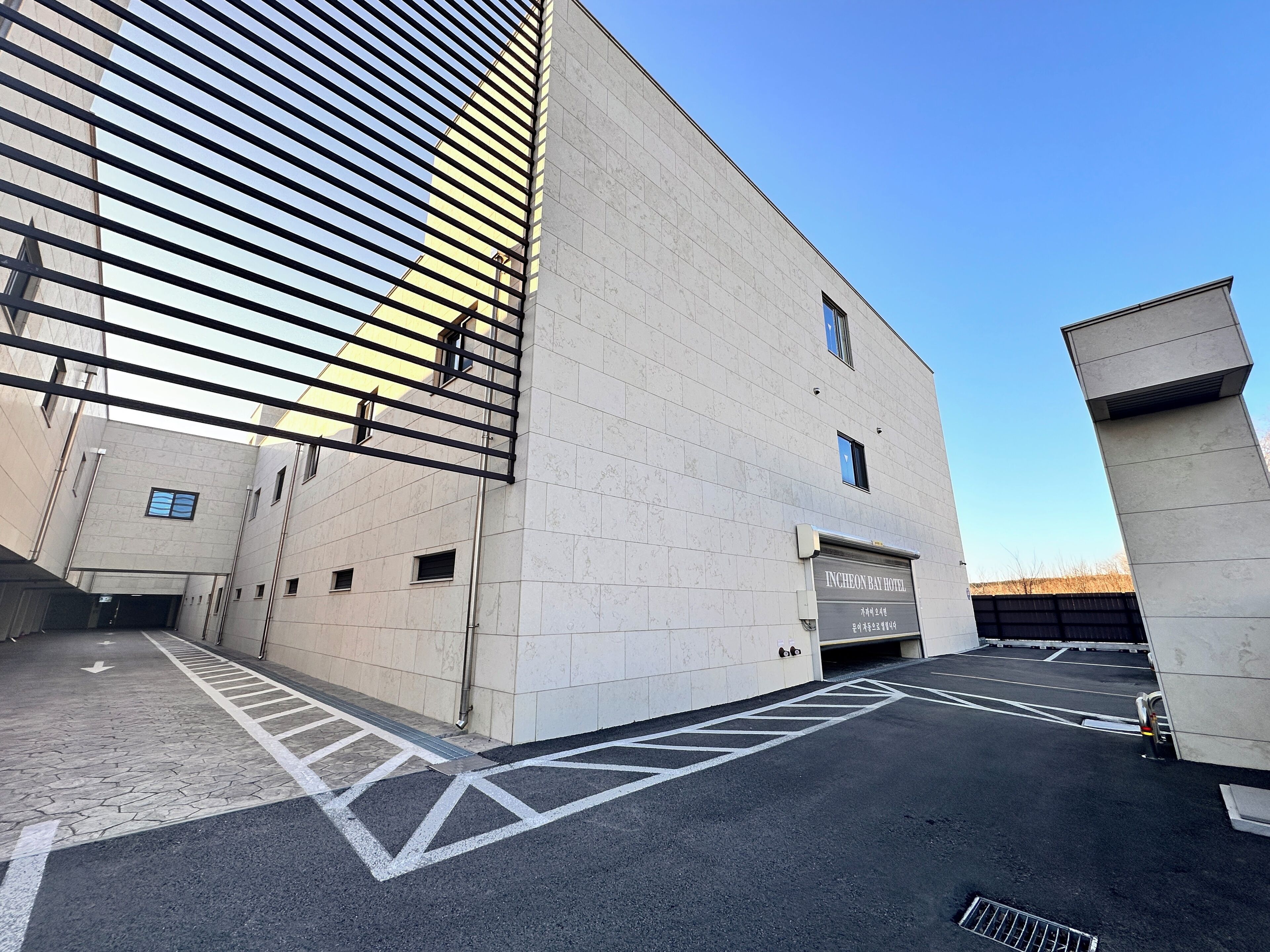 A modern building with a sign for Incheon Bay Hotel, featuring a clean, geometric design and a parking area with directional arrows.