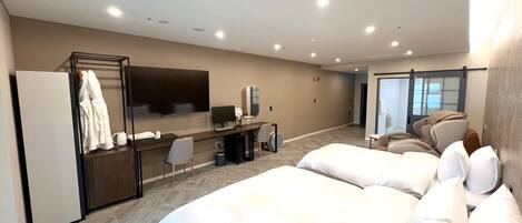 A hotel room with a bed, a desk with a computer, a TV, and a seating area with a massage chair.