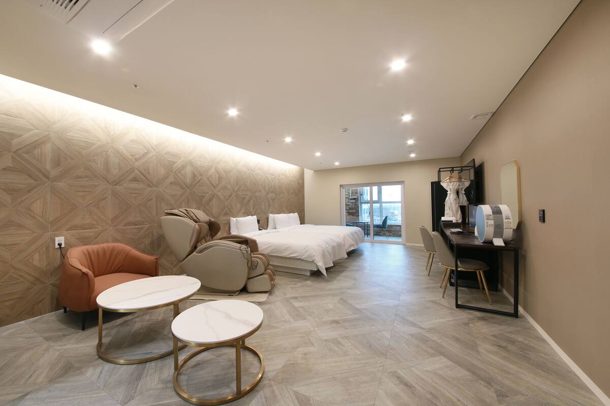 A modern hotel room with a large bed, a seating area with two round tables, a sofa, and a mirror.