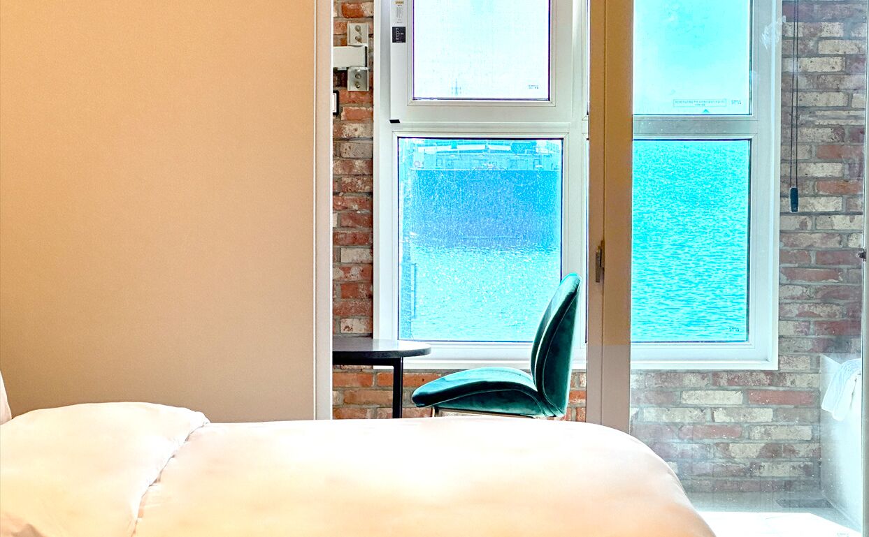 Ein Schlafzimmer mit einem großen Bett, einem Sessel und Meerblick durch ein Fenster.