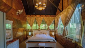 A bedroom with a wooden ceiling, a bed, two bedside tables, a window with curtains, and a chandelier.