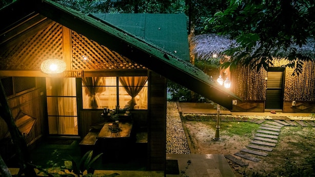 A wooden cabin with a sloped roof, a porch with a table and chairs, and a small garden area with a pathway.