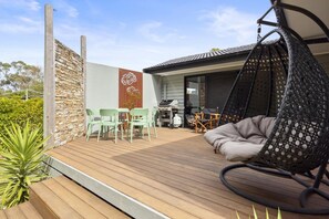 A wooden deck with outdoor furniture, a hanging chair, and a stone wall with a decorative panel.