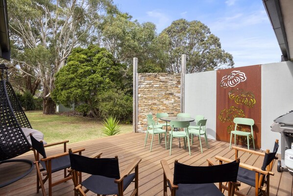 An outdoor patio with wooden deck, green chairs, and a stone wall.
