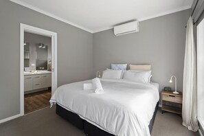 A bedroom with a large bed, bedside table, and a nightstand with a lamp.